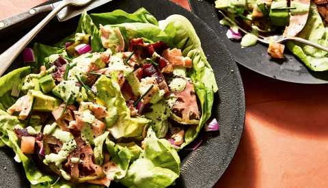 salad with lettuce, salmon, bacon, avocado and onion on plate; part of another plate with salad on it is to the upper right