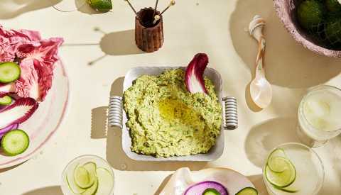 Hummus in bowl on table, surrounded by glasses and other food