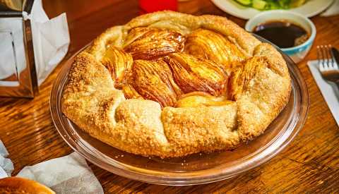 whole pear galette on glass plate on a wood table with a cup of coffee and restaurant napkin dispenser