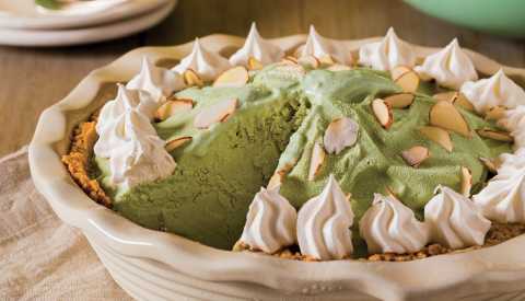 gotcha matcha ice cream pie from egg rolls & sweet tea cookbook decorated with whipped cream and almond slivers with a slice taken out of it