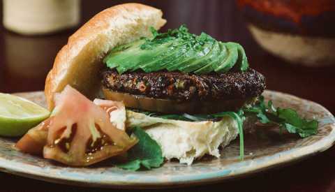 black bean quinoa burger with avocado on it on plate; cut up tomato next to it