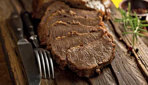 brisket cut into slices with fork and knife next to it on wood