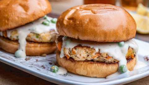 two chicken potpie burgers with gravy on buns on a white plate