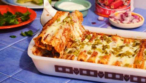 smoked cheddar and chicken manicotti enchiladas in pan, spatula scooping some out