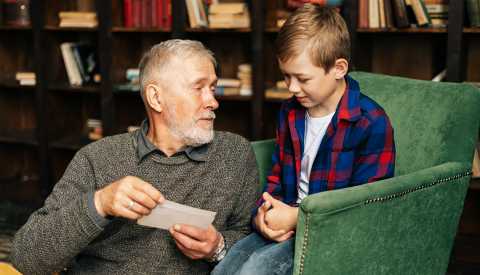 Grandfather talking with grandson at home in cozy room home study with a background of bookshelves. Grandfather talking with grandson at home in a room with background of bookshelves.