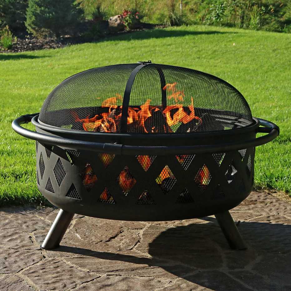 a black firepit sits lit near a green yard
