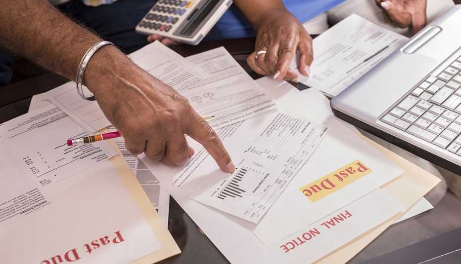 close up of the hands of a couple pointing at overdue monthly bills spread out on living room table. 