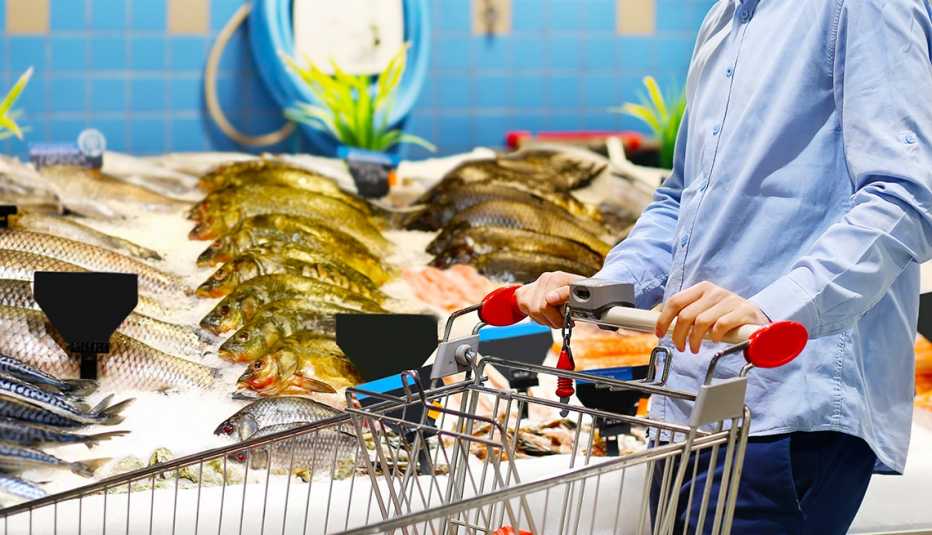 a man pushing a supermarket shopping cart past the fresh fish counter 