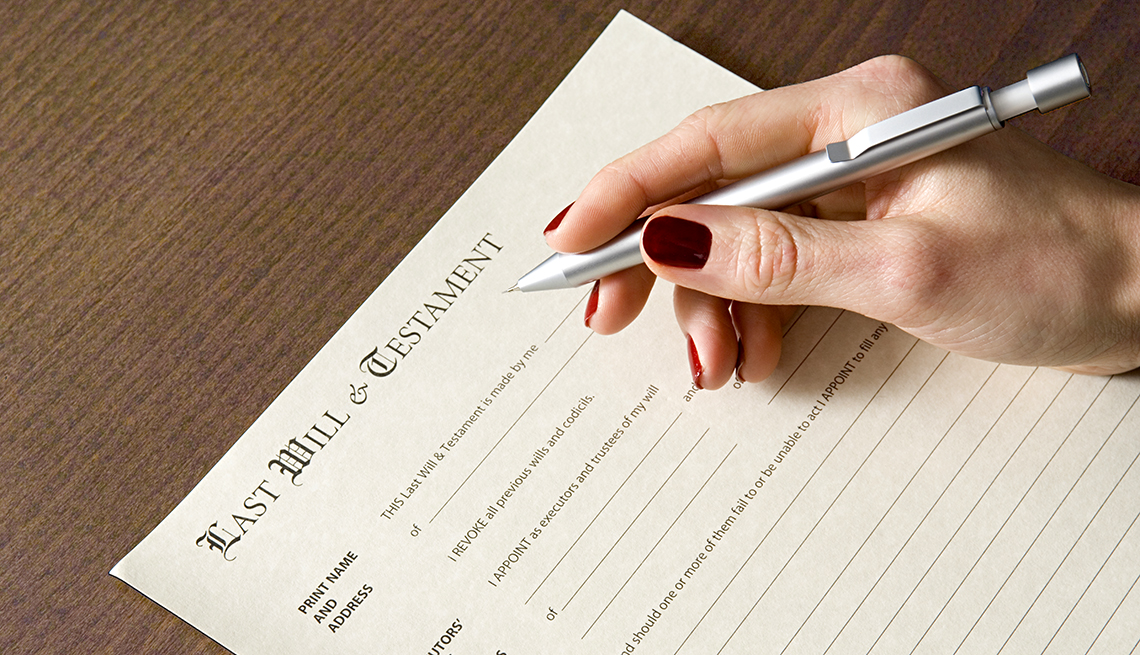 A women's hand holds a pen over a blank last will and testament document