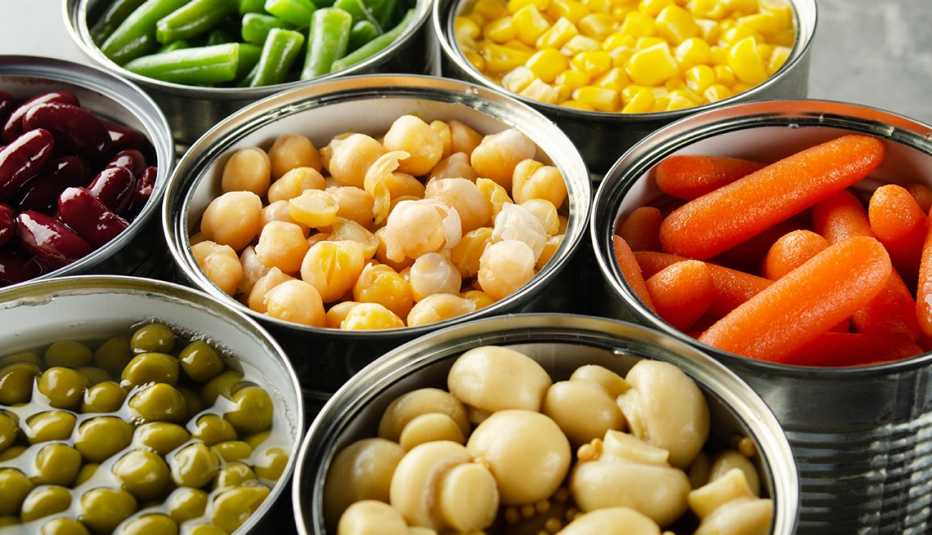 Canned vegetables in opened tin cans on kitchen table. 