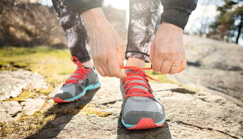 an older persons hands shown as they bend down to tie their sneaker while exercising outside