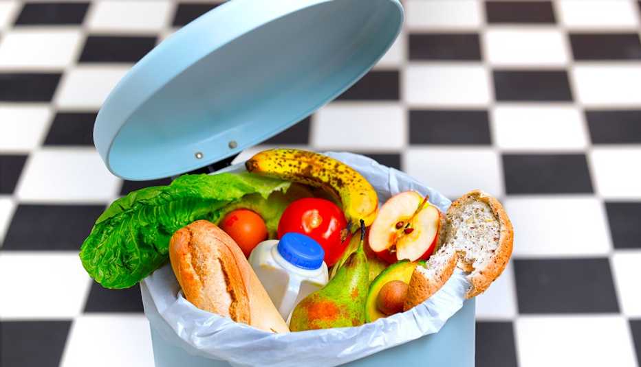 A kitchen trash can full of stale bread, wilted lettuce, uneaten fruit and spoiled milk. 
