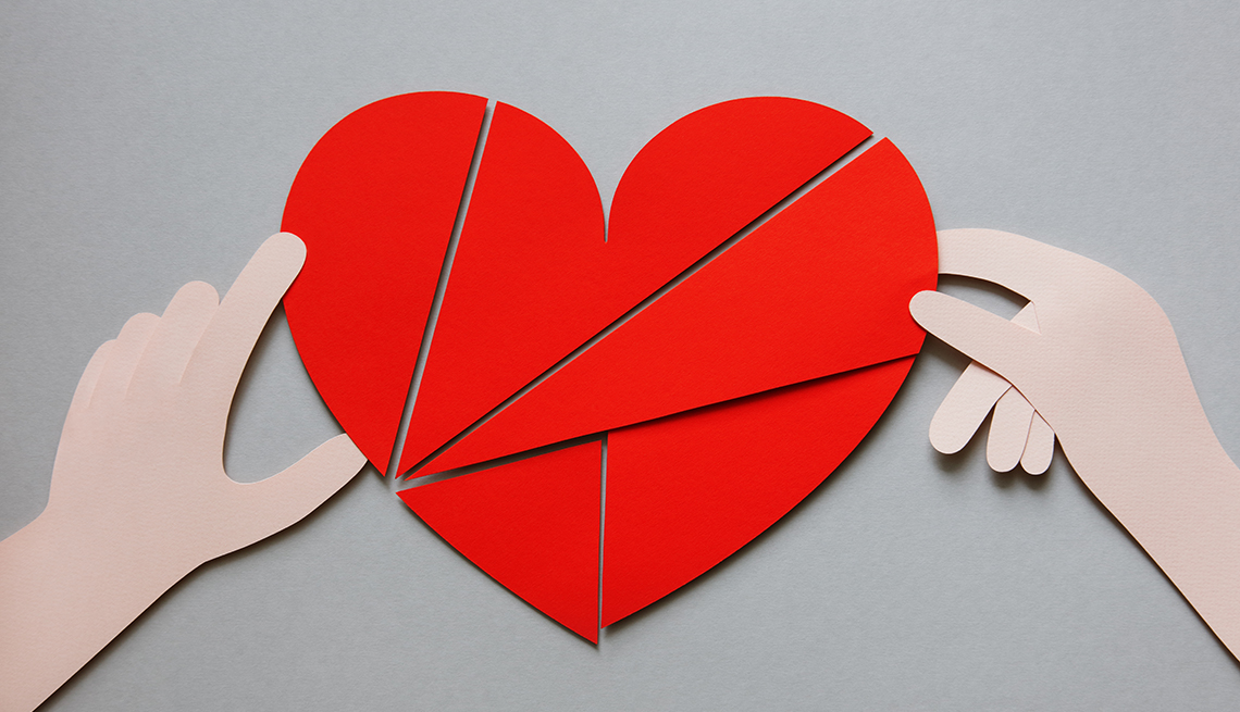 illustration of paper cut-out hands holding together red slivers of a paper heart on a gray background