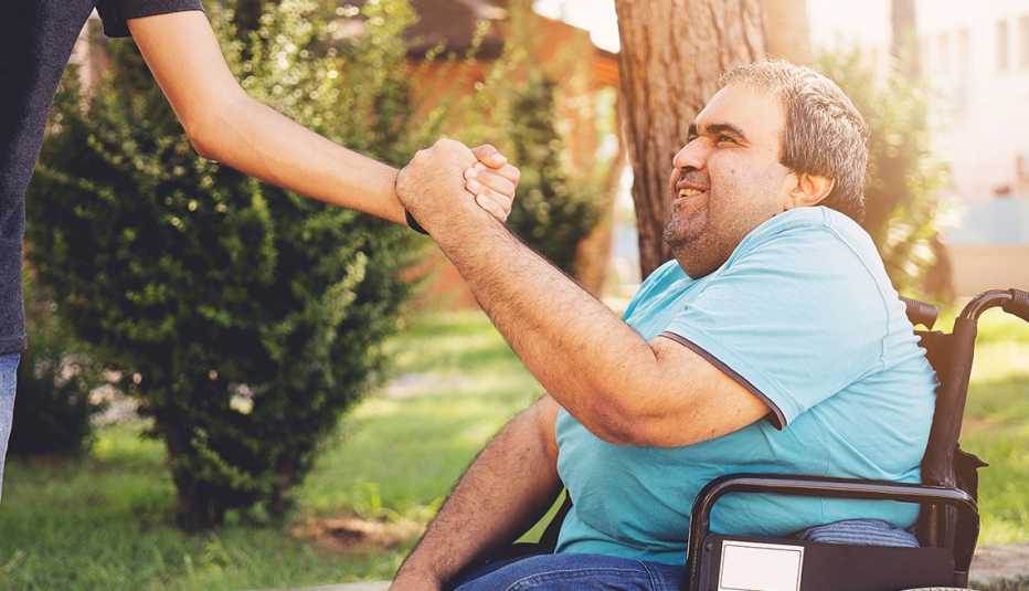 outdoor casual setting shows a smiling man in a wheelchair reaching up shaking hands with an unseen person