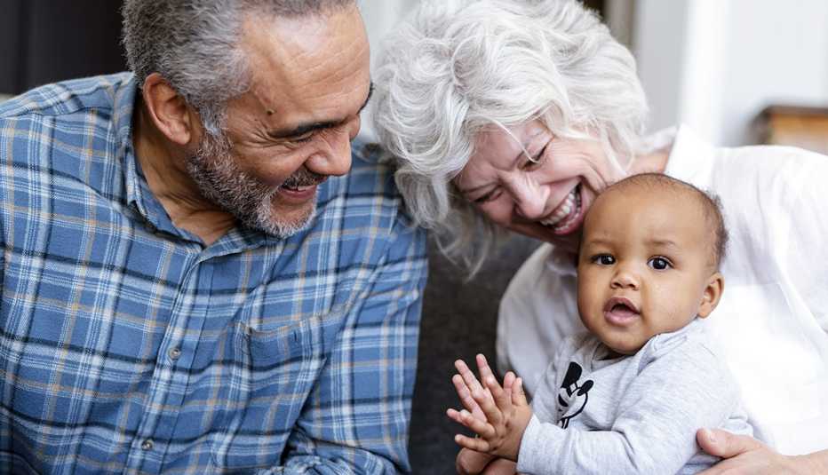 Grandparents laughing and holding a clapping baby while sitting on the couch. 