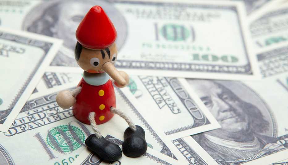miniature pinoccho wooden toy with long nose sitting on a pile of hundred dollar bills