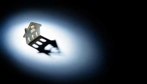 A flatl wooden house stands in a circle of light and casts a shadow against a dark background A flatl wooden house stands in a circle of light and casts a shadow against a dark background