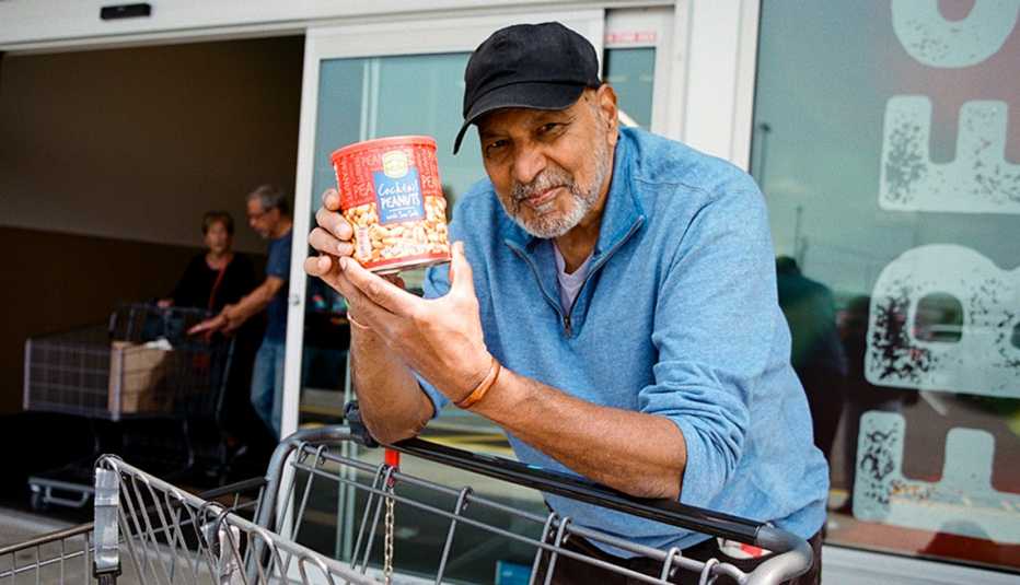 man shows us a can of nuts leaning on grocery cart in front of a supermarket
