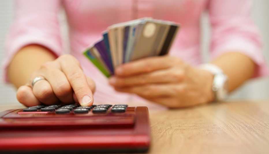 soft-focus woman holding handful of credit cards is adding up spending on a red calculator in foreground