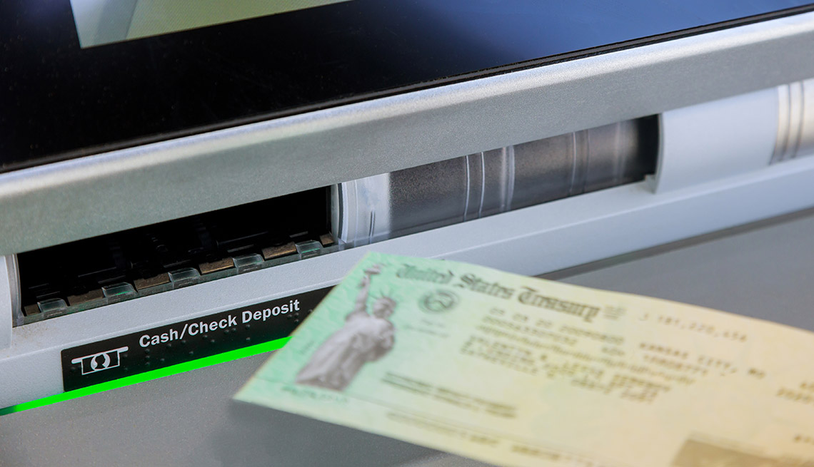 a stimulus check is being fed into the check deposit open slot of a bank ATM 
