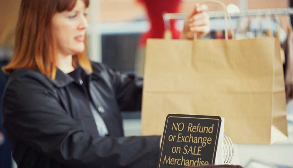 shopper making purchase at store counter that displays a sign about the return policy: "No refund or exchange on sale merchandise"