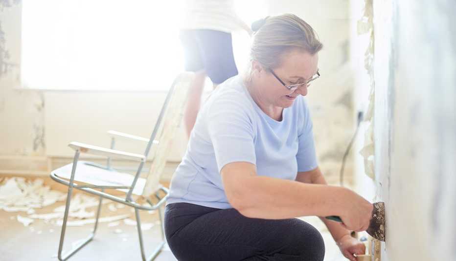 Homeowner kneeling and using a scraper to strip off old wallpaper to make home improvements