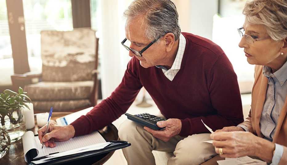 senior couple writing notes to keep track of budget expenses while sitting on the living room sofa