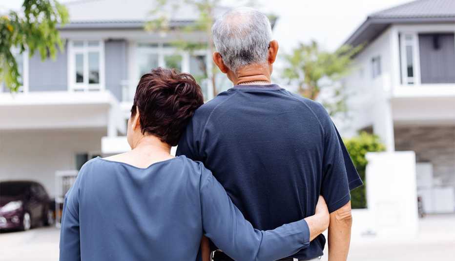 a couple standing the woman has her arms around the mans back as they look at houses