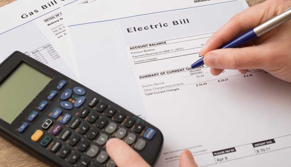 close up of hand writing next to calculator and electric bill on table close up of hand writing next to calculator and electric bill on table