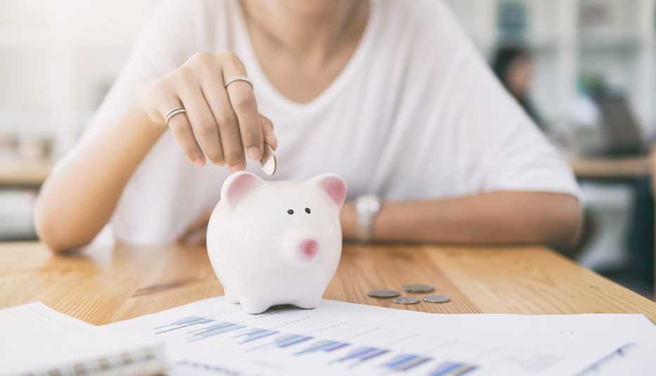 woman putting money in white piggy bank