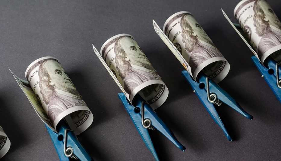 Groups of one hundred dollar bills clipped with blue clothespins run in a diagonal line across a gray background. 