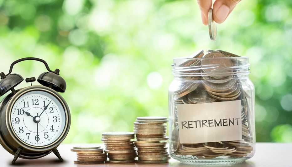 hand putting coins in glass jar with retro alarm clock  for time to money saving for retirement