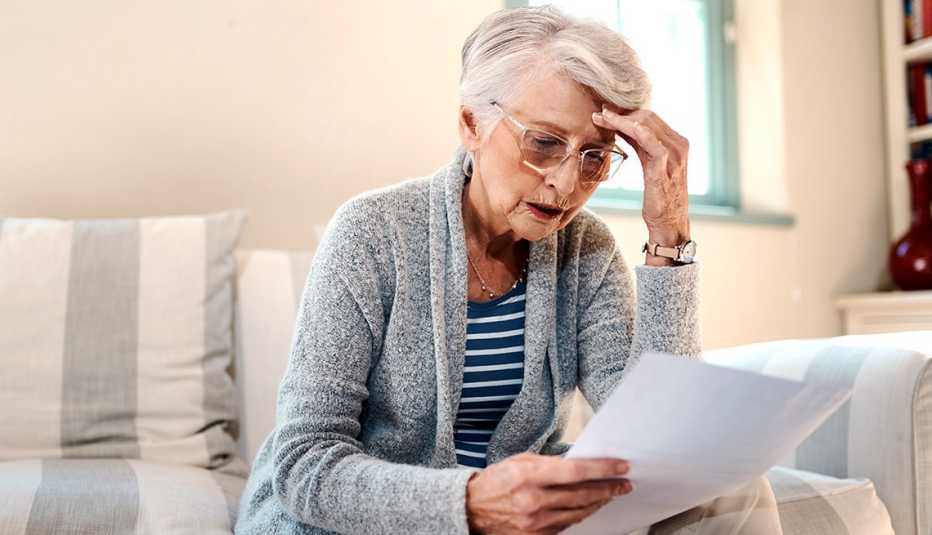 woman looks worried and holds fingers to her temple as she concentrates on reading a piece of paper
