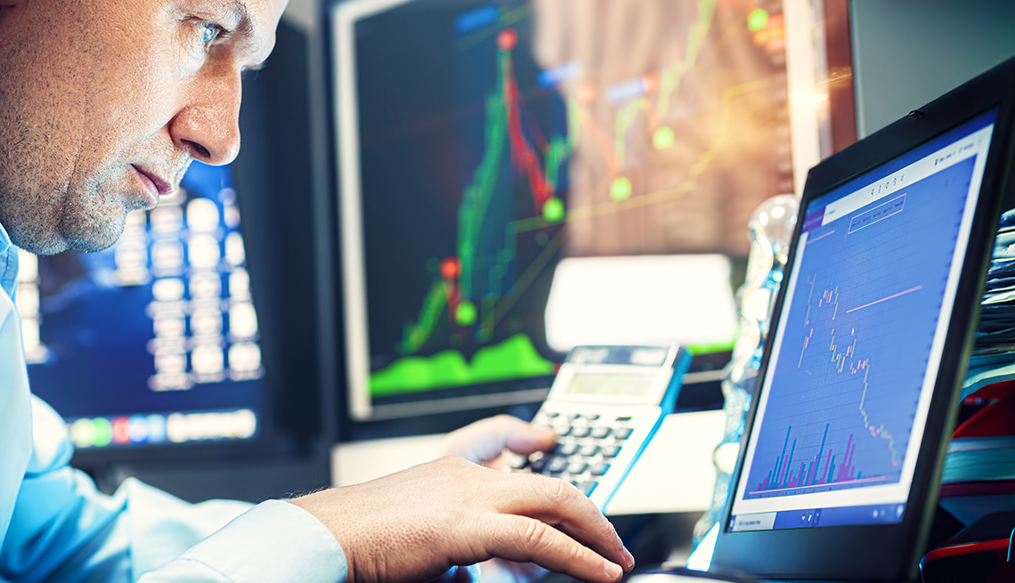 A man looking closely at financial investment and economic charts displayed across three screens