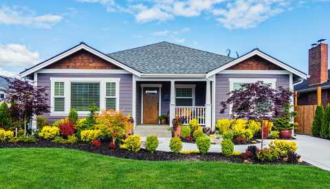 grey single-level home with white trim; sidewalk leading to driveway; gorgeous grass in front, along with mulch where red, yellow and green shrubs and trees sit