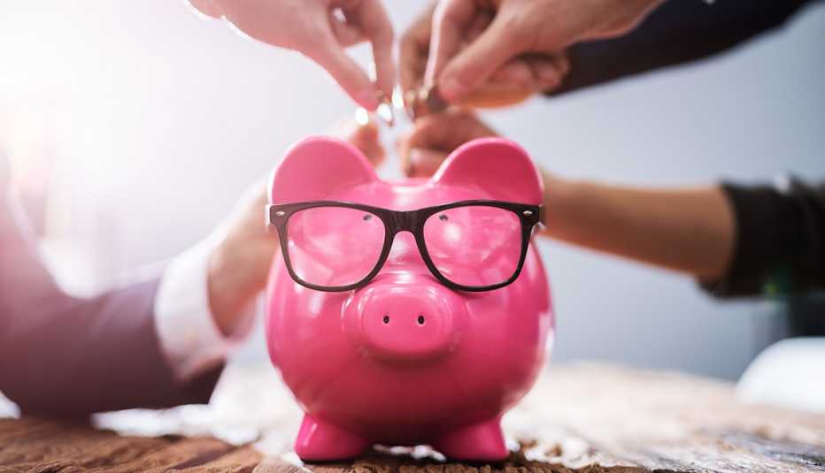 hands reaching into frame inserting coins into pink piggy bank