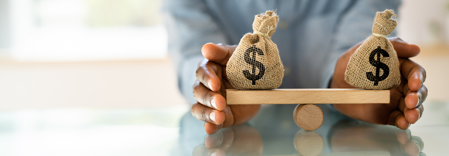 hands surrounding a balanced seesaw of bags of cash showing equal amounts