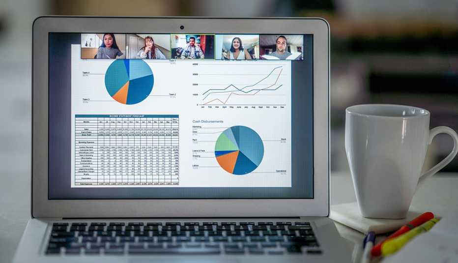 An open laptop sits next to a cup of coffee — the laptop screen displays a group of people meeting remotely to discuss finances and stock market investments.