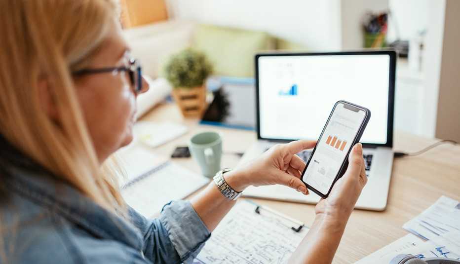 profile of a woman looking at financial charts on a mobile phone with more notes and financial information on desktop and laptop screen