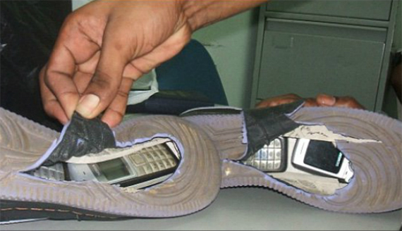 a hand holds open a tear in the bottom sole of a shoe sitting sideways on a table to reveal two hidden cell phones in each shoe a hand holds open a tear in the bottom sole of a shoe sitting sideways on a table to reveal two hidden cell phones in each shoe