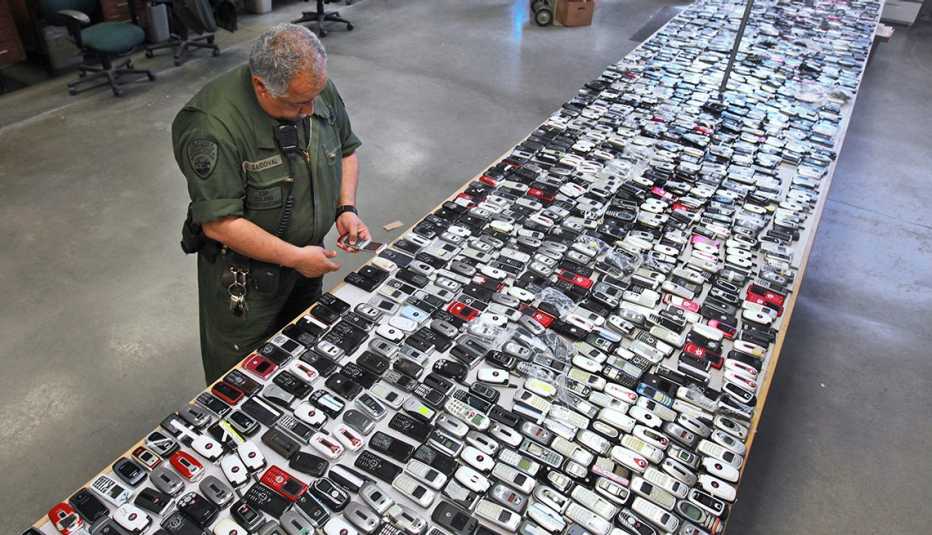 a prison guard inspects a long table entirely covered with contraband cellphones confiscated from inmates a prison guard inspects a long table entirely covered with contraband cellphones confiscated from inmates