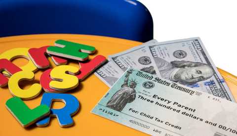 US Treasury illustrative check for child tax credit on table with 3 hundred dollar bills and colorful letters US Treasury illustrative check for child tax credit on table with 3 hundred dollar bills and colorful letters