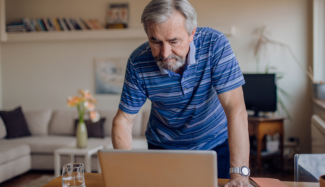 man standing over open laptop looks at computer screen