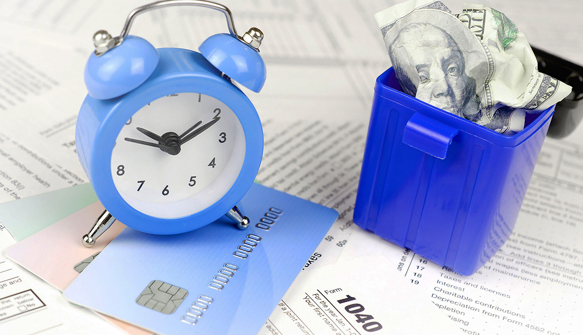1040 Individual income tax return form with blue alarm clock on credit cards and crumpled hundred dollar bill in trash bin