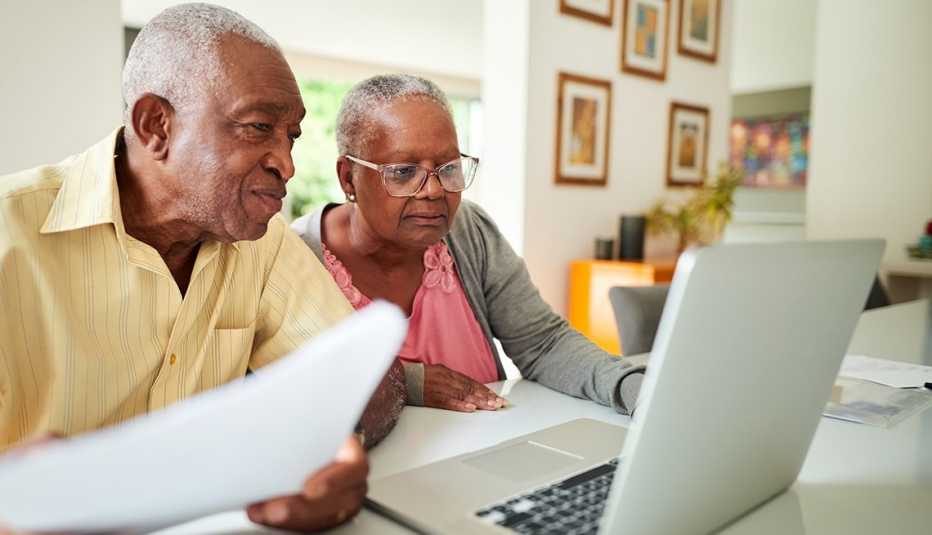 couple in home setting work together on financial paperwork and look at laptop computer screen