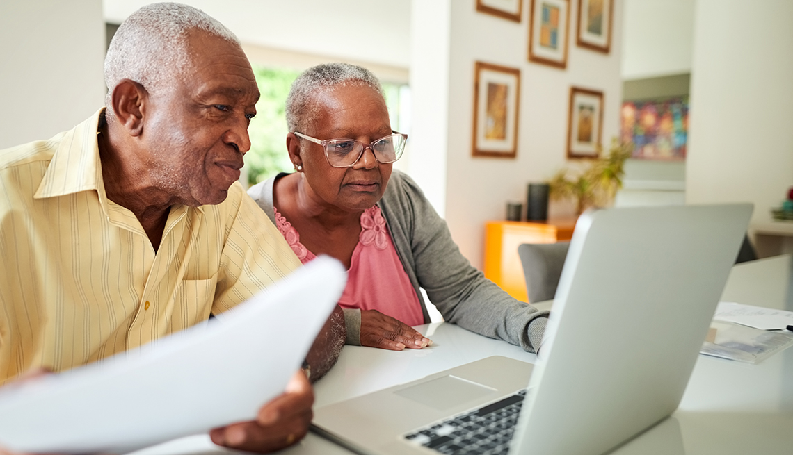 couple in home setting work together on financial paperwork and look at laptop computer screen