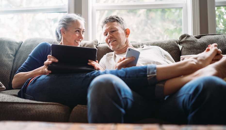 A couple using their mobile devices on a couch easily downloading the AARP Now app A couple using their mobile devices on a couch easily downloading the AARP Now app