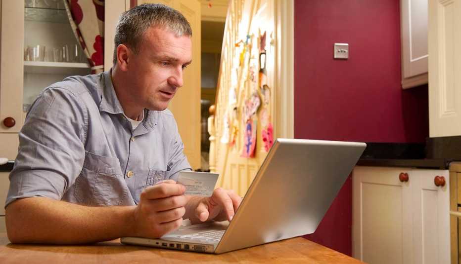 Hombre sentado frente a una computadora con tarjeta de crédito en la mano