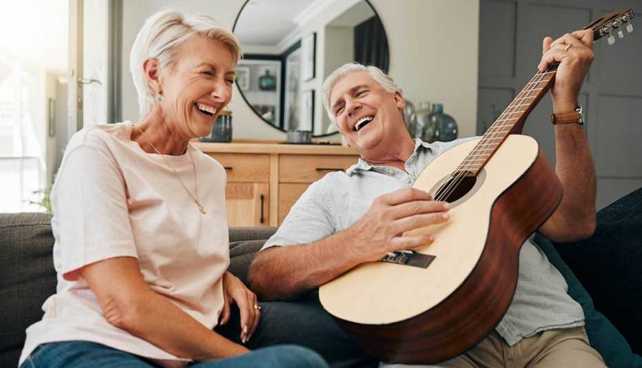 Man playing guitar man on a couch playing guitar with a laughing woman sitting next to him