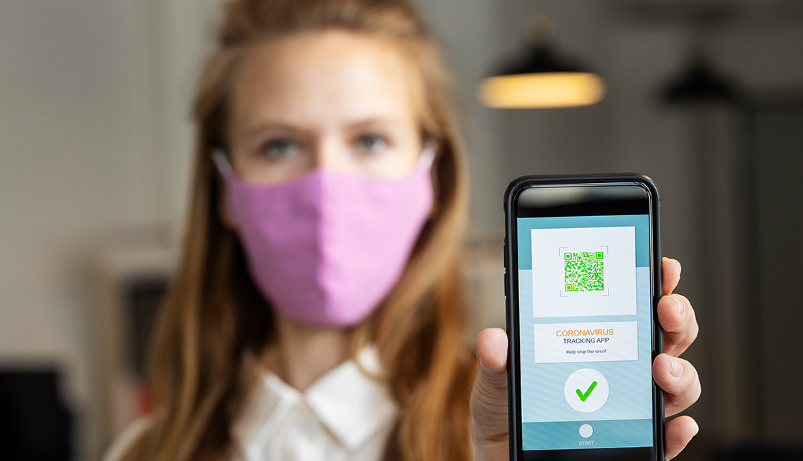 A woman wearing a mask holds up her phone